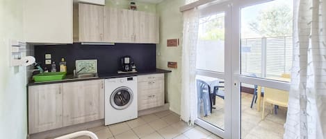 A compact kitchen with a washing machine, a coffee maker, and a dining area with a table and chairs.