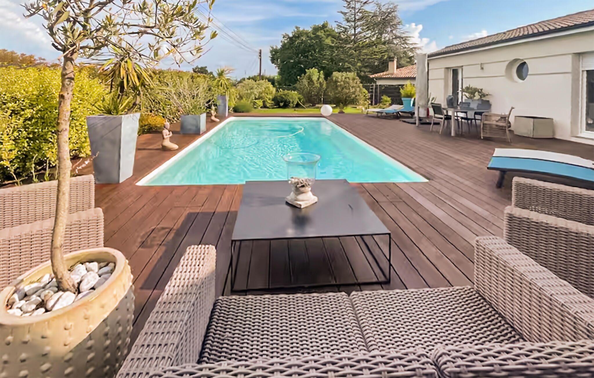 Une terrasse en bois avec une piscine, des meubles en osier et une statue.