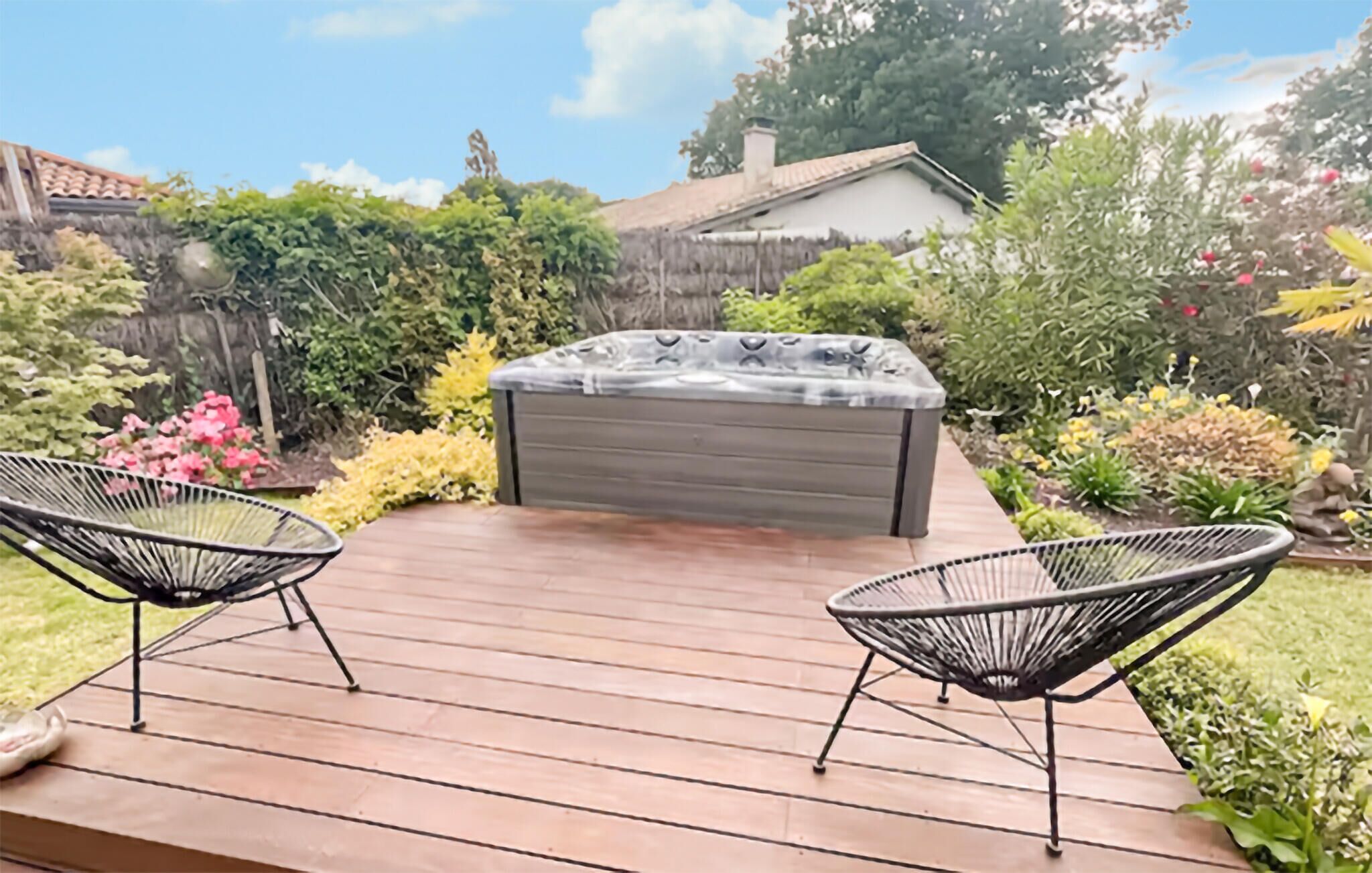 Een houten terras met een jacuzzi en twee stoelen, omgeven door een tuin met diverse planten en bloemen.
