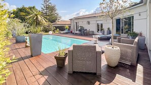 Terraza de madera con piscina, mobiliario de mimbre y plantas en macetas.
