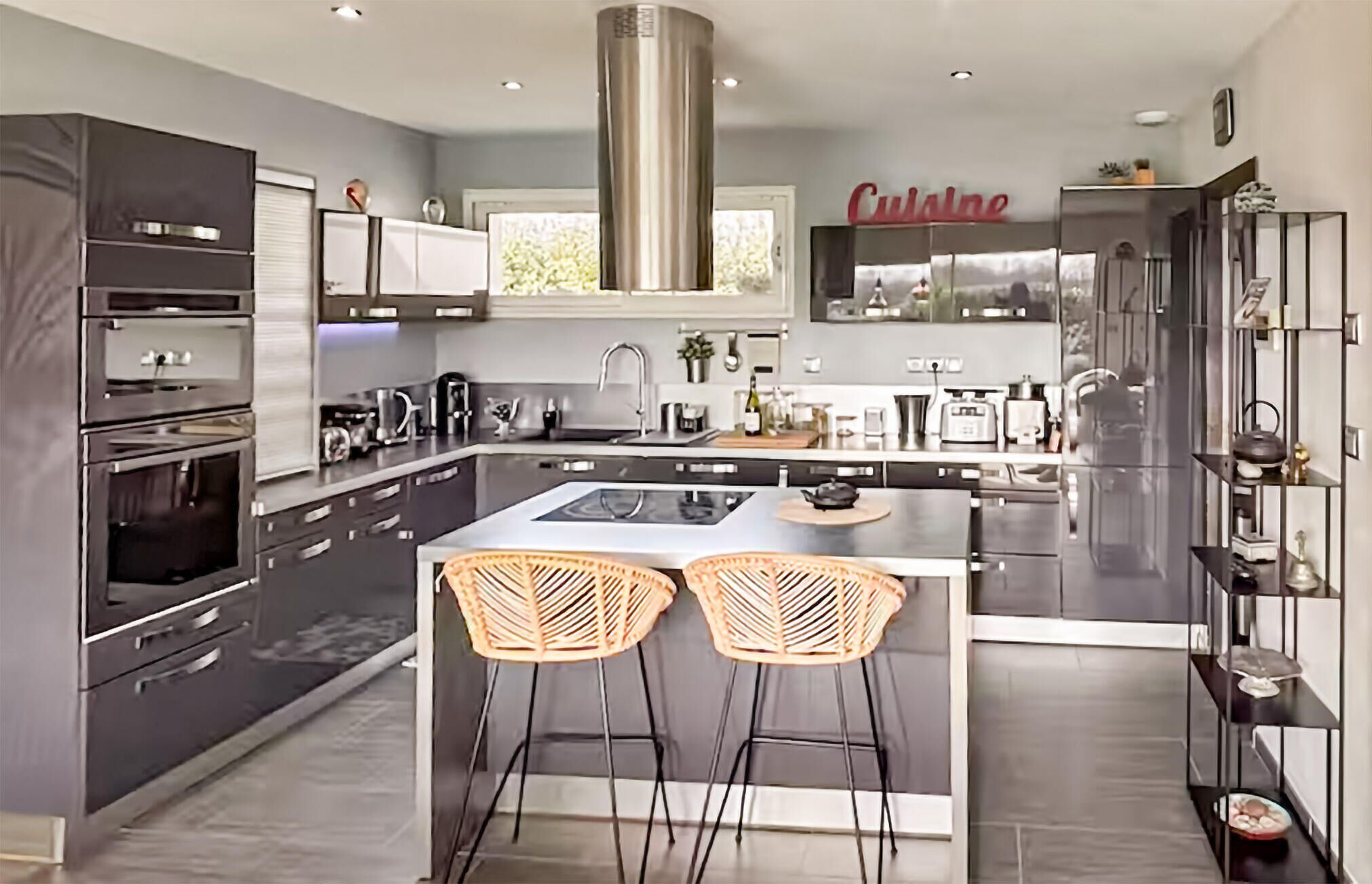 Uma cozinha moderna com uma ilha central, dois banquetes, fornos embutidos e um exaustor de aço inoxidável.