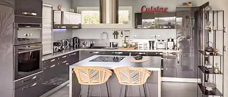 Uma cozinha moderna com uma ilha central, dois banquetes, fornos embutidos e um exaustor de aço inoxidável.