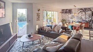Una sala moderna con sofá, mesa de centro y televisor, un comedor con sillas y mesa, y un balcón con piscina.