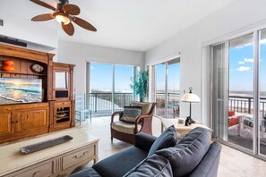 A spacious living area with a balcony, wooden furniture, and a television. - Oceanfront Condo W/ Double Wide Balcony & Heated Pool! 🏖️ (Cocoa Beach)