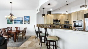 Una cucina moderna con forno a microonde, forno e elettrodomestici in acciaio inossidabile. C'è un'area pranzo con un tavolo e sedie in legno.