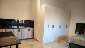 Ein modernes Schlafzimmer mit Bett, Nachttisch, Kleiderschrank und einer Küchenzeile mit Schränken und Arbeitsplatte.