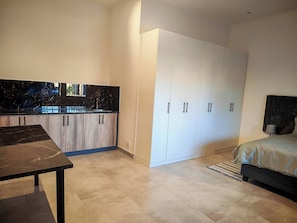 A modern bedroom with a bed, a nightstand, a wardrobe, and a kitchen area with cabinets and a countertop. - Room-king Superior Studio Room With En-s (Cape Town)
