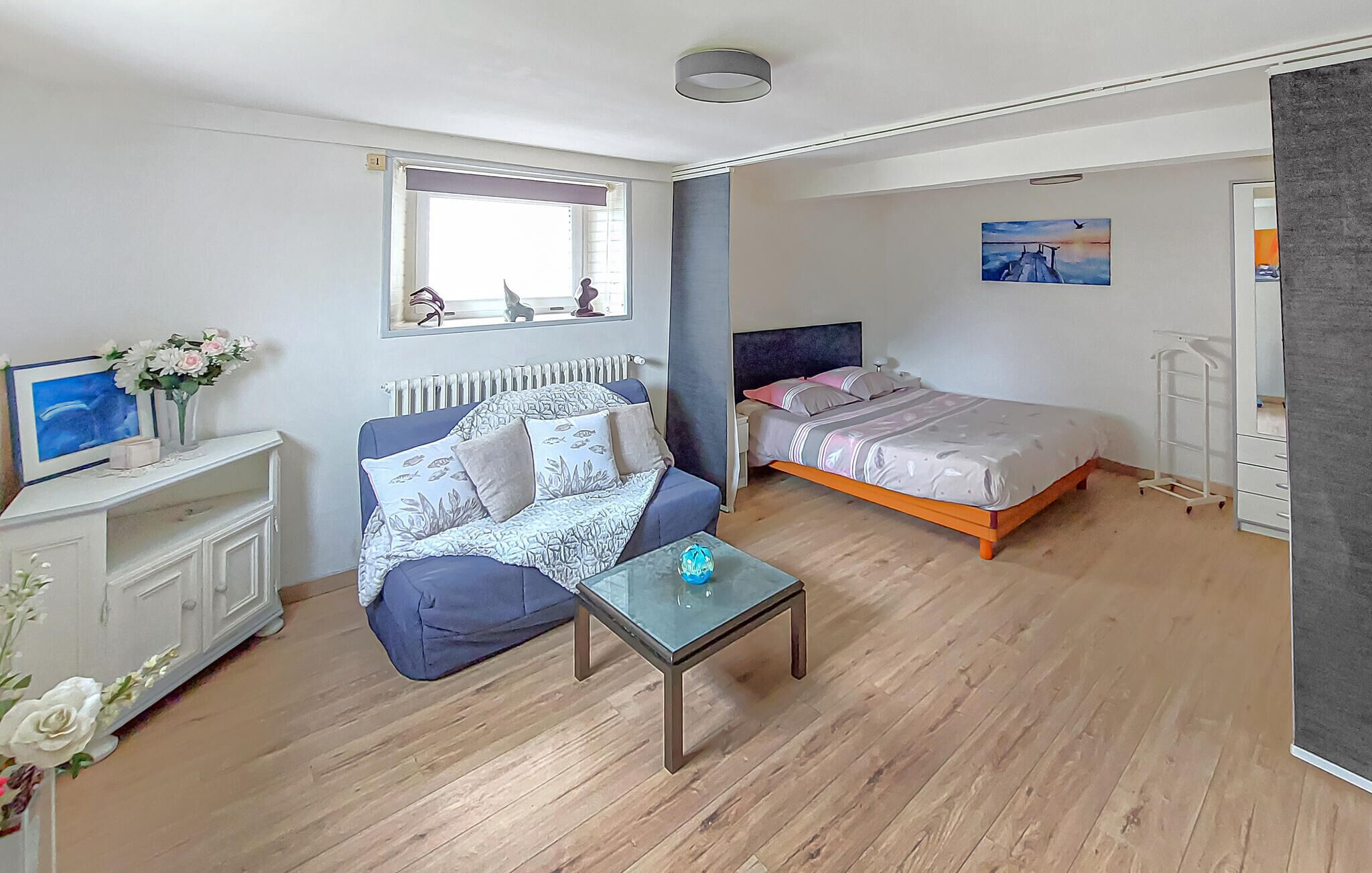 Una habitación pequeña con sofá, cama, una mesita y un radiador.