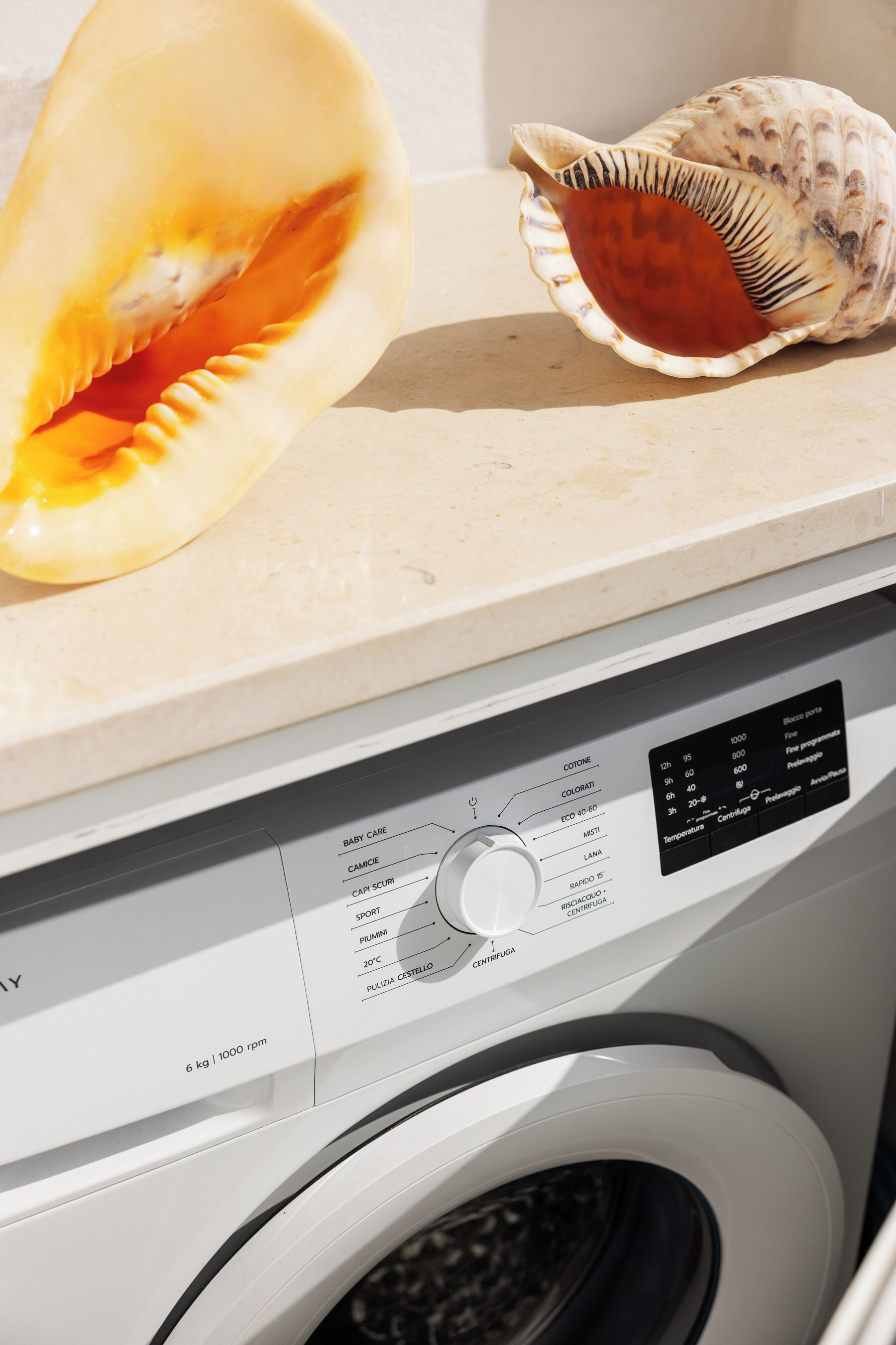 A washing machine with a control panel, a partially opened shell, and a seashell on top.
