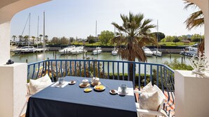 A balcony with a table set for breakfast overlooking a marina with boats and palm trees.