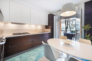 A modern kitchen with dark cabinets, a gas stove, and a dining area with a table and chairs. - Cattolica Master Beach - Riviera Collection (Cattolica)