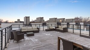 Eine Dachterrasse mit Gartenmöbeln, einem Holztisch und einem Geländer.
