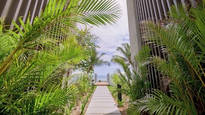 A pathway leading to a beach, flanked by tall buildings and lush greenery. - Les Estivales Beachfront Suites & Penthouses, LOV (NORTH)