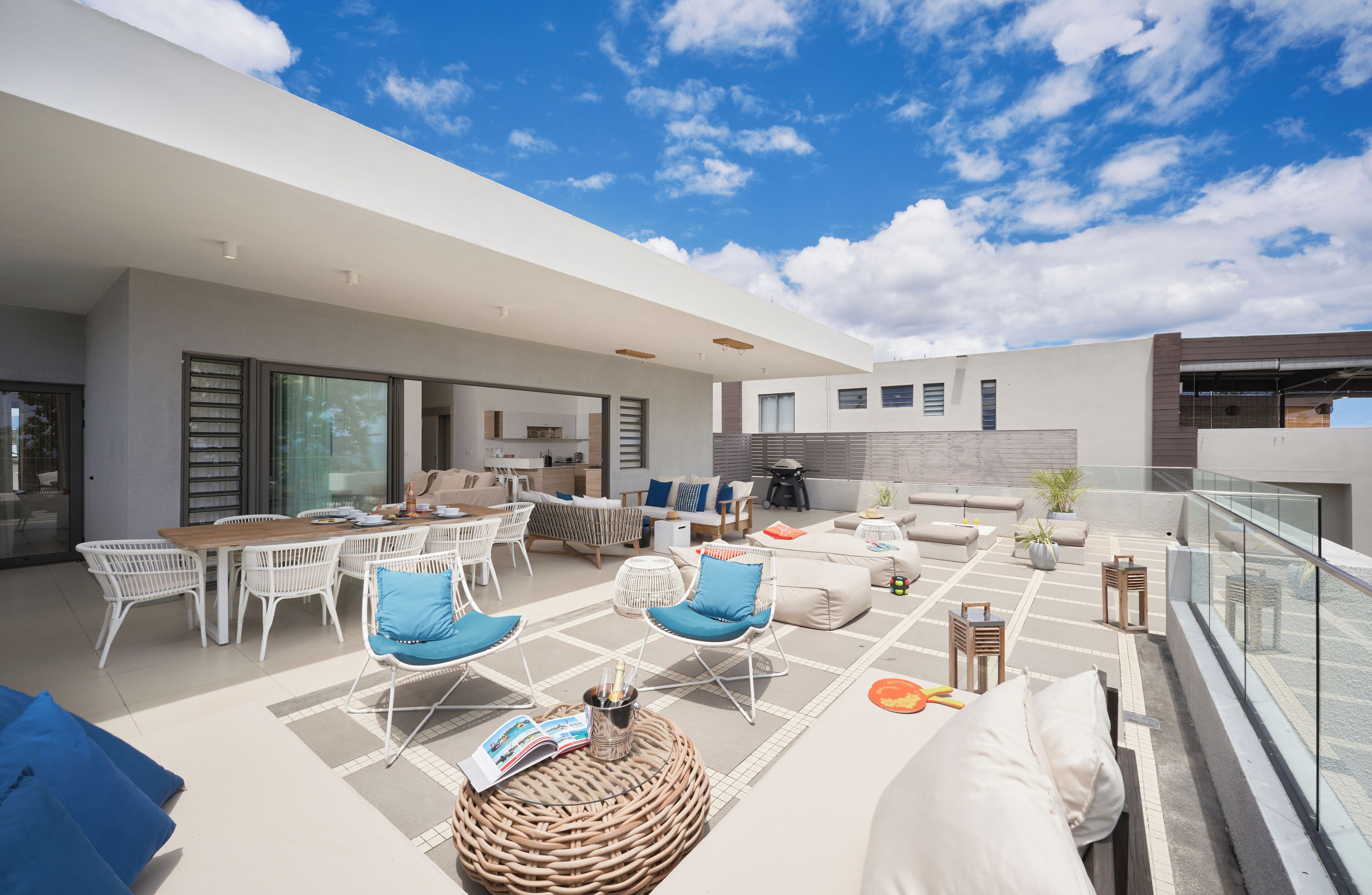 A modern outdoor living space with a dining area, lounge chairs, and a glass balustrade.