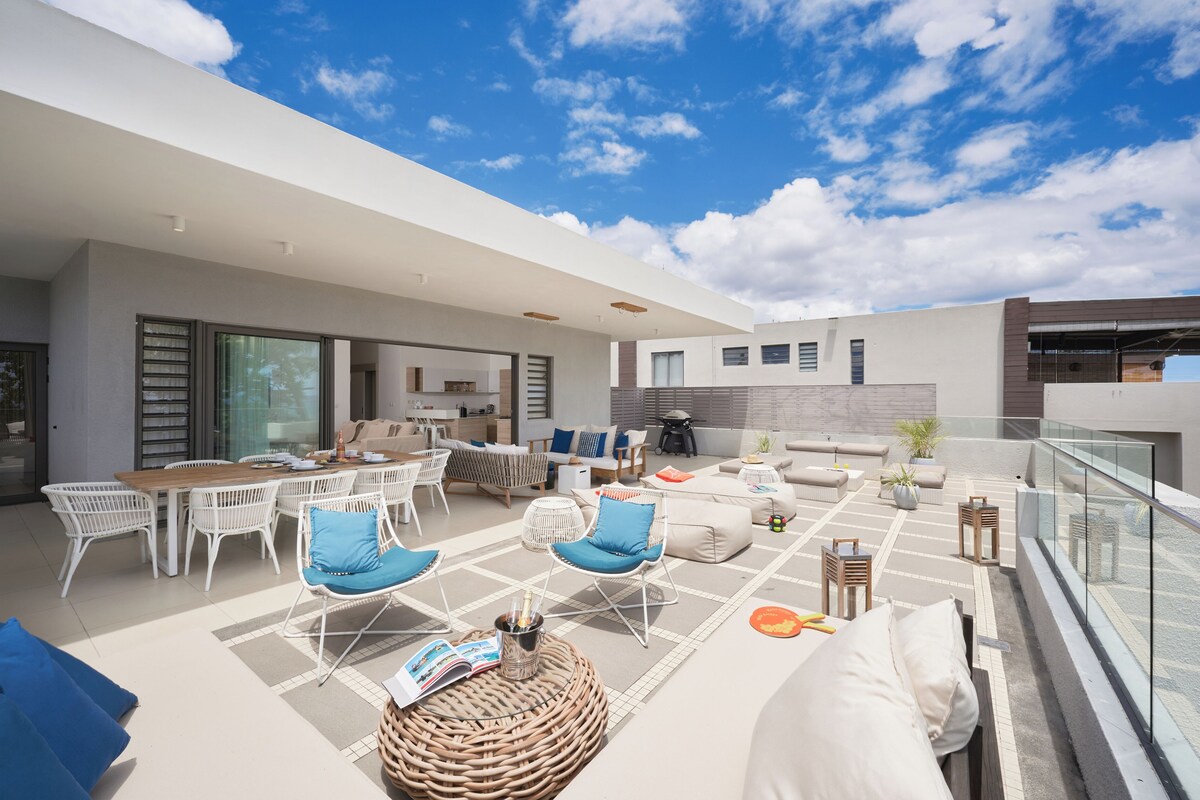 A modern outdoor living space with a dining area, lounge chairs, and a glass balustrade.
