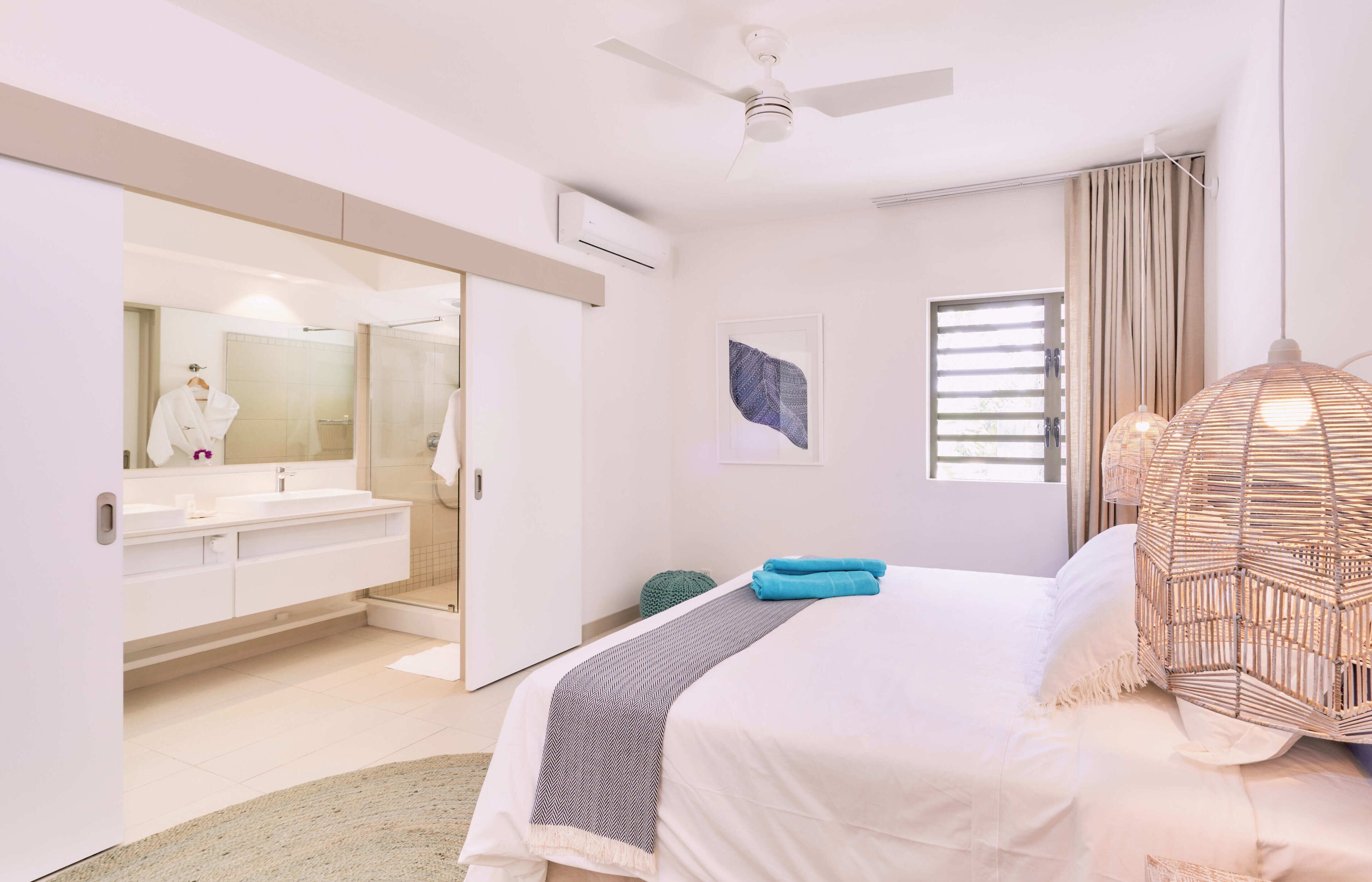 A bedroom with a bed, a bedside lamp, a mirror, a window with curtains, and a ceiling fan.