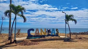 Una spiaggia con un cartello che riporta la scritta 'CANAS' e palme.