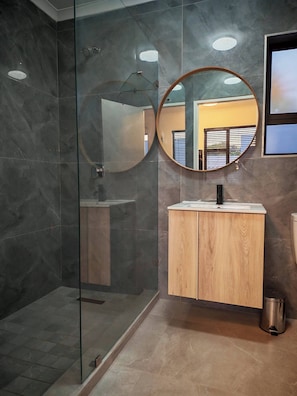 A modern bathroom with a glass-enclosed shower, a wooden vanity, and a round mirror. - Room-king Deluxe Cottage Room (Cape Town)