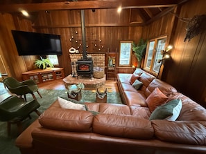 A cozy living room with a leather sofa, a fireplace, a flat-screen TV, and wooden walls.