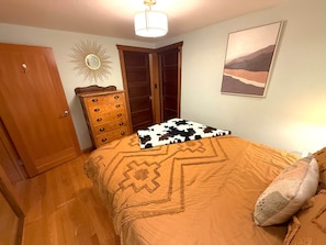 A bedroom with a bed, a dresser, a mirror, and a painting on the wall.