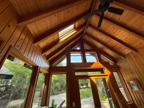 A wooden interior with a sloped ceiling, large windows, and a ceiling fan.