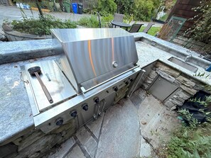 An outdoor kitchen with a stainless steel grill, a sink, and a stone countertop.