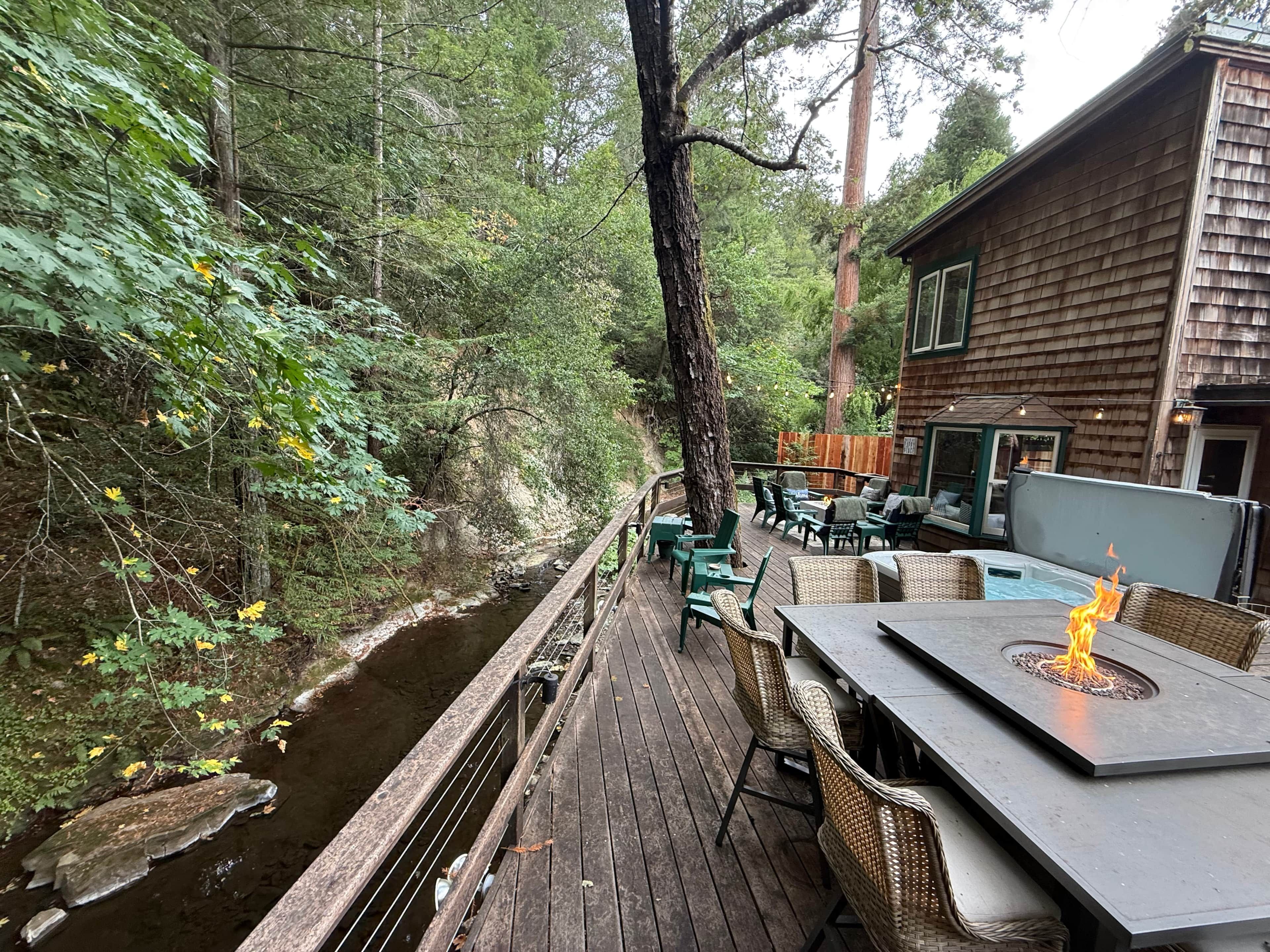 A wooden deck with outdoor seating and a fire feature, surrounded by dense forest.