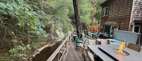 A wooden deck with outdoor seating and a fire feature, surrounded by dense forest.