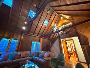 A wooden interior with a sofa, a dining table, and a staircase leading to an upper level.