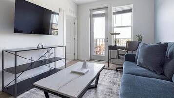 Un soggiorno moderno con divano, tavolino, TV a parete e un balcone con vista.