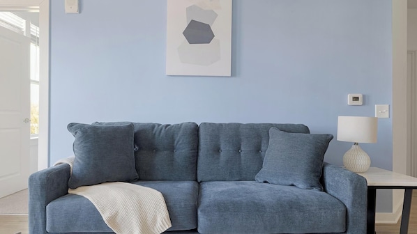 A room with a blue sofa, a white lamp, and a framed abstract artwork on the wall.