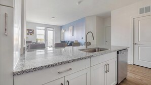 Una cocina moderna con encimeras de granito, un lavamanos de acero inoxidable y armarios blancos.