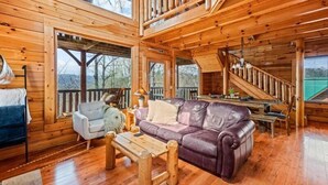 Ein Holzblockhaus im Inneren mit einer Couch, einem Esstisch und einer Treppe.
