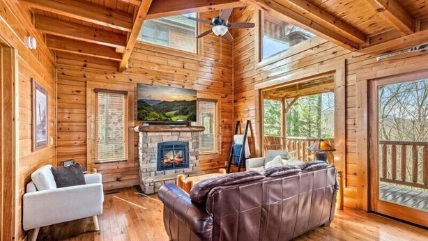 Ein rustikales Holzhaus-Interieur mit Kamin, Ledersofa, weißem Sessel und einem an der Wand befestigten Fernseher.
