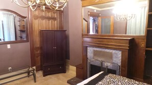 A room with a wooden wardrobe, a fireplace, a bed with a patterned bedspread, and a large mirror above the fireplace. - Spacious Victorian Mansion with 8-bedroom in marvelous Denver with AC (Denver)