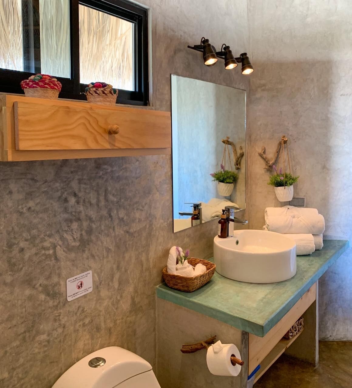 A bathroom with a round sink, a mirror, and a window with blinds.