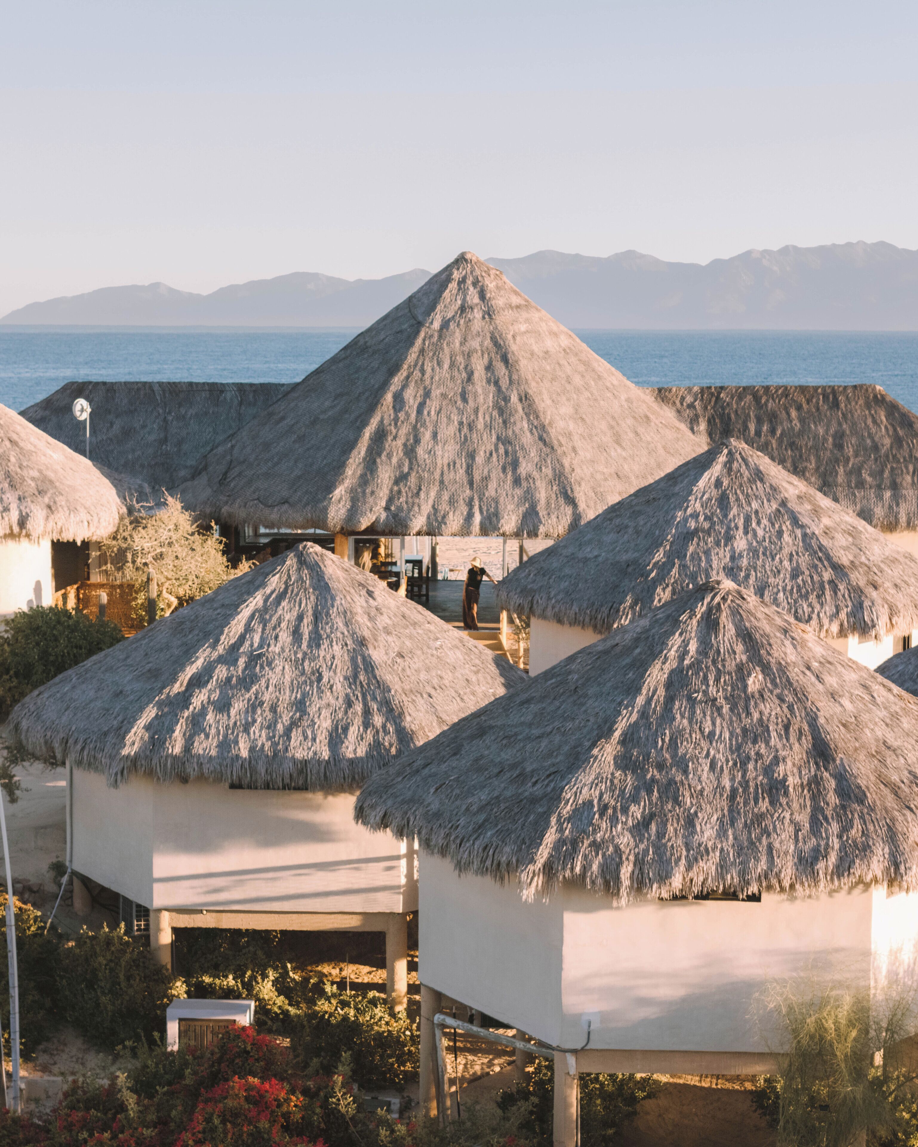 Thatched-roof huts with a view of the sea and mountains in the background.