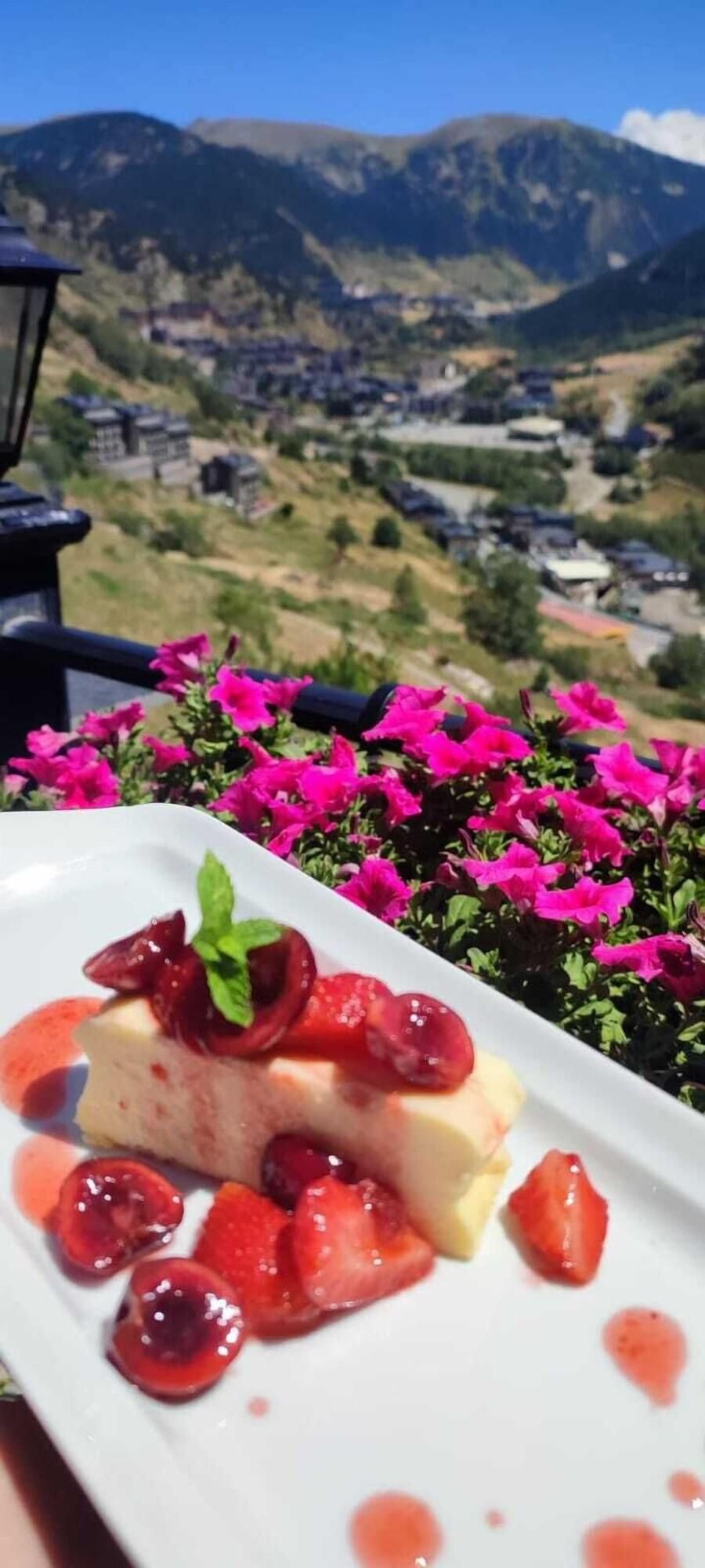 A dessert plate with strawberries and a mint garnish, set against a backdrop of pink flowers and a mountainous landscape.