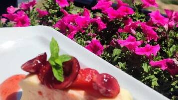 Un plato de postre con fresas y una ramita de menta, sobre un fondo de flores rosadas y un paisaje montañoso.