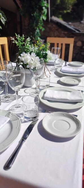A table set outdoors with white tablecloths, clear glassware, and a vase with white flowers. - Ransol (Ransol)