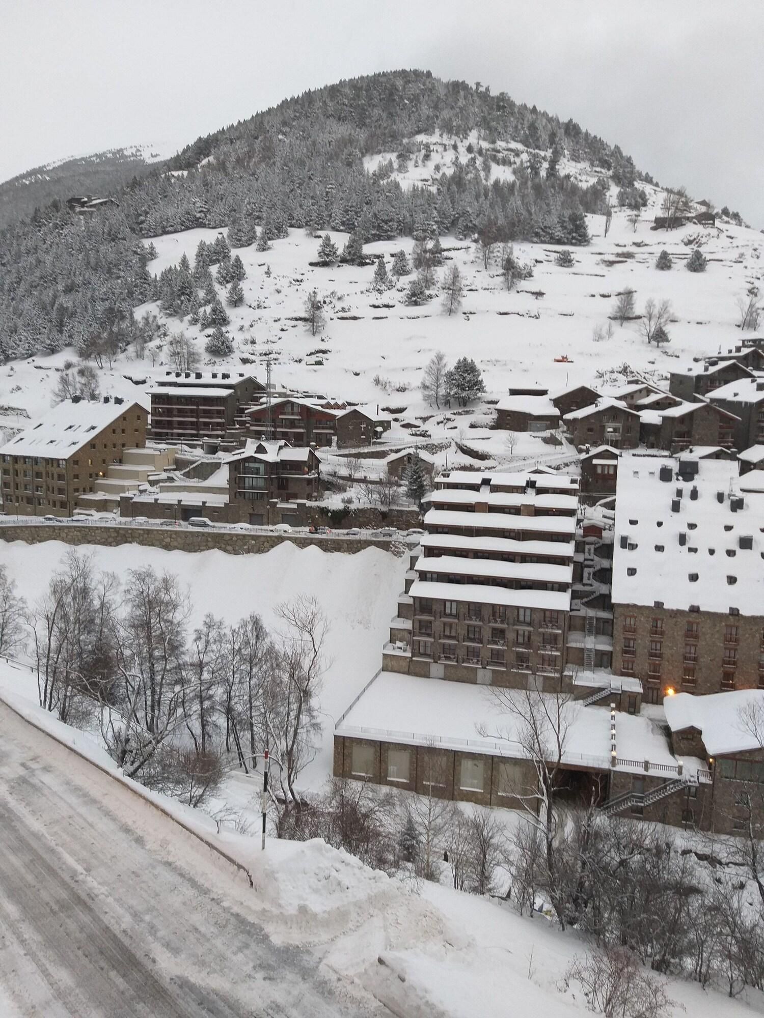 Un quartier résidentiel enneigé, avec des immeubles à plusieurs étages, dont certains sont dotés de balcons, et un paysage vallonné en arrière-plan.