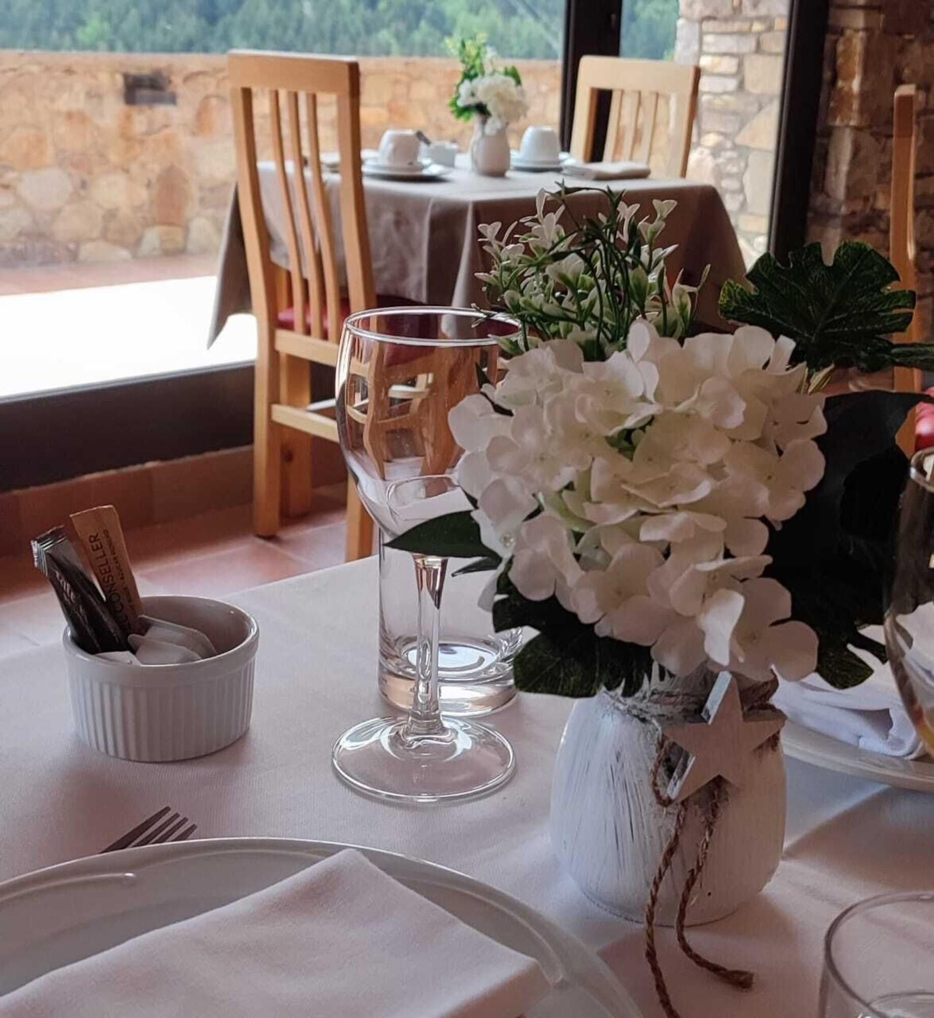 A dining table set with white tablecloth, a vase of white flowers, and a glass of water.