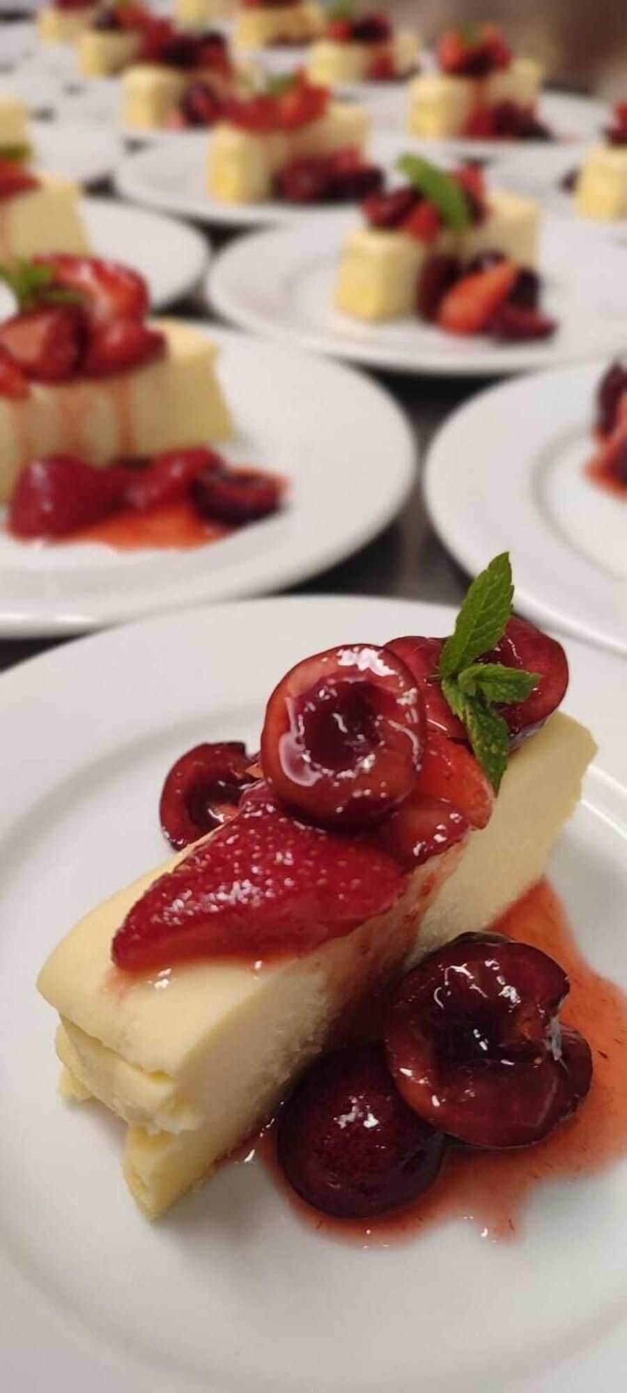 A dessert plate with a slice of cheesecake topped with cherries and a mint leaf.