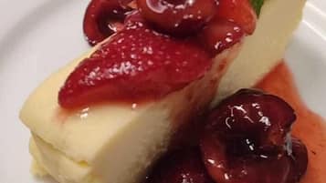 A dessert plate with a slice of cheesecake topped with cherries and a mint leaf.