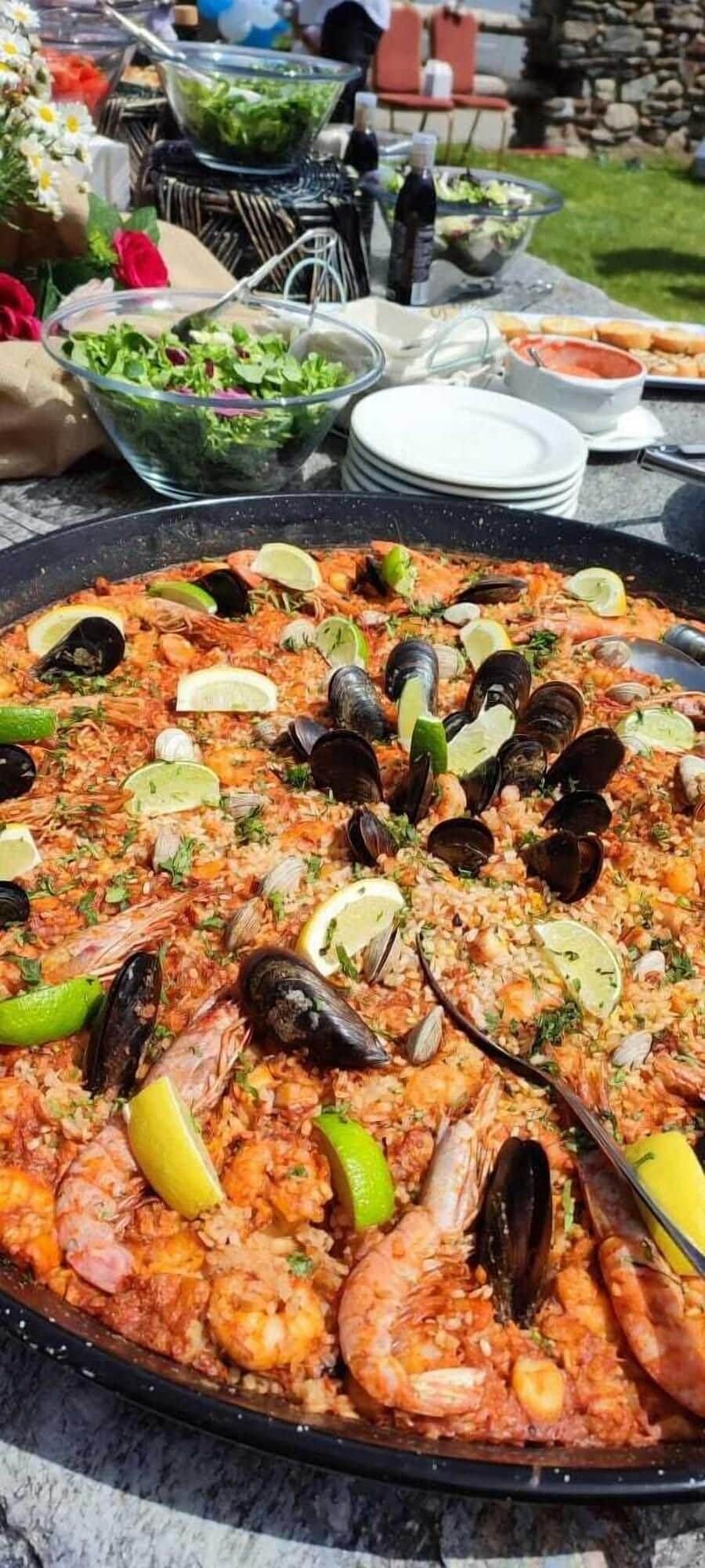 Una paella de mariscos generosa sobre una mesa con guarniciones y bebidas diversas.