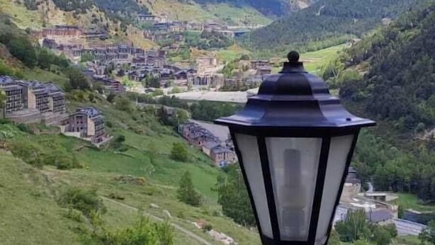 A scenic view of a mountainous landscape with a village and a black street lamp in the foreground.