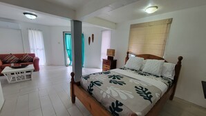 Un dormitorio con una cama de madera, una mesita de noche blanca, un sofá rojo y un suelo blanco.