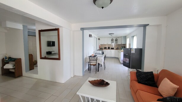Una sala de estar con una mesa de centro blanca, un sofá naranja, un comedor con mesa y sillas, y una cocina con armarios y electrodomésticos.
