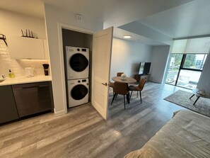 Apartament modern amb cuina, zona de dinar i saló. Hi ha dues rentadores superposades, una taula de dinar amb cadires i una finestra gran que ofereix vistes al carrer.