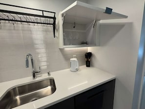 Una cuina moderna amb un obrador d'acer inoxidable, taulell blanc i una prestatgeria per a vi integrada sobre l'obrador.